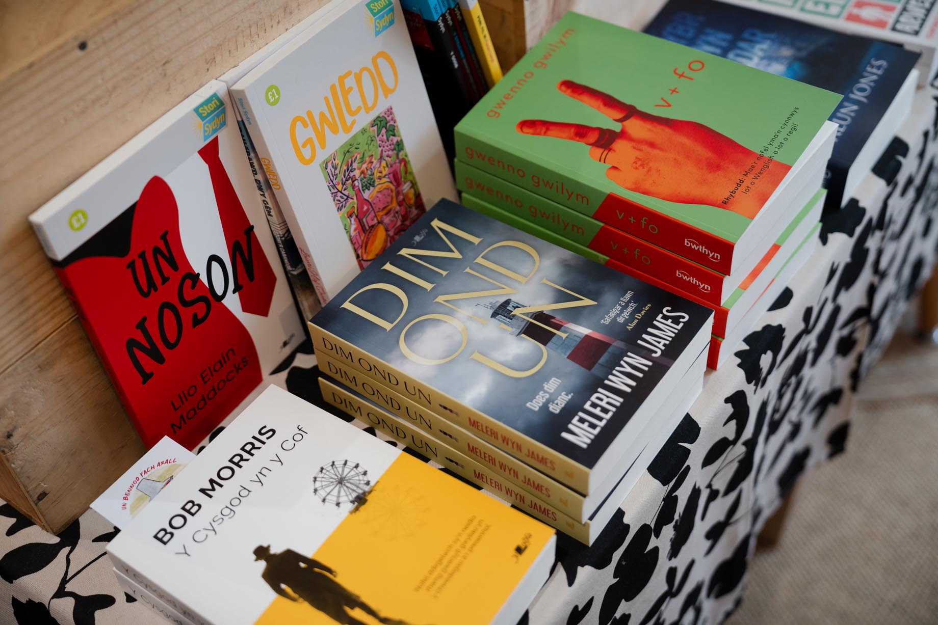 Llyfrau Cymraeg wedi eu pentyru ar y fwrdd arddangos mewn siop lyfrau