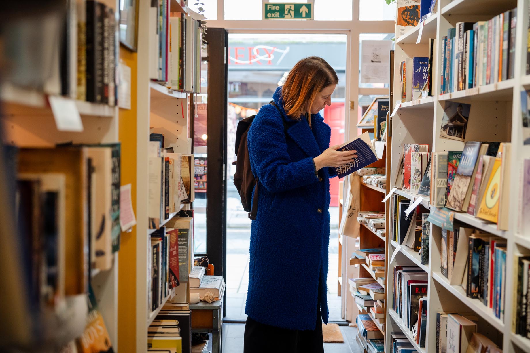 Menyw mewn cot las yn darllen llyfr mewn siop lyfrau